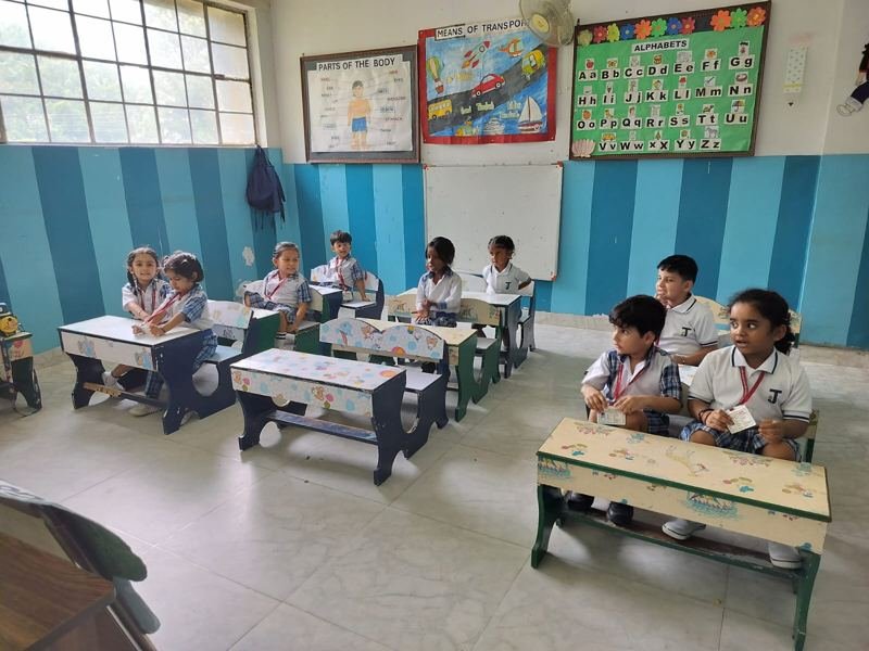 Young Joyland Montessori School children seated on small benches in a blue classroom, some holding their ID cards