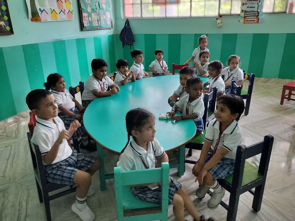 Joyland Montessori School children seated around a teal table in their classroom, smiling and looking up