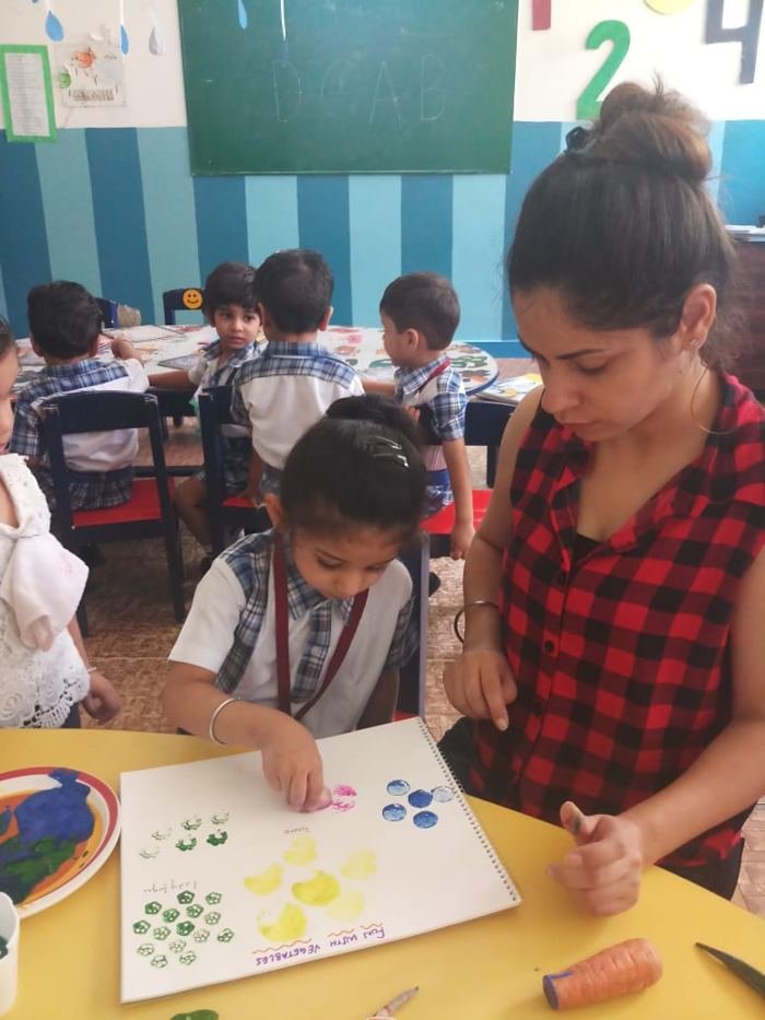 A Joyland child painting with fingertips beside a teacher