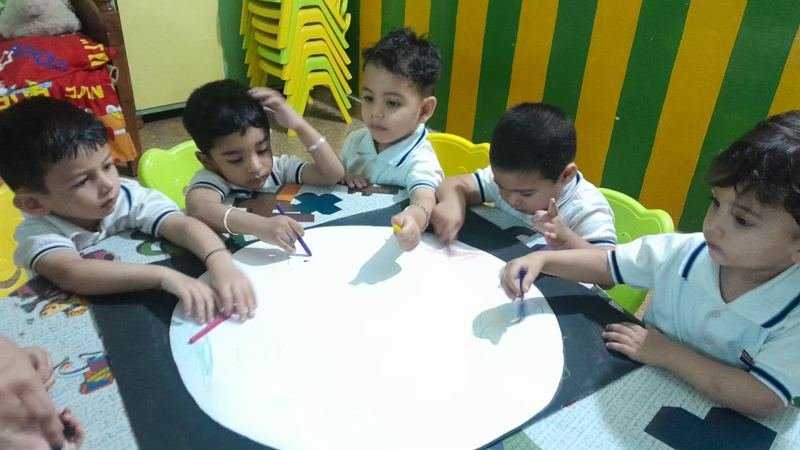 Five Joyland Montessori School children drawing with crayons on a large circle of paper