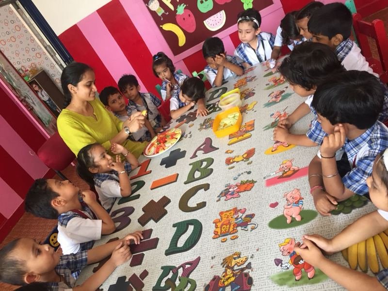 Children and a teacher seated around a long table covered with an alphabet cloth
